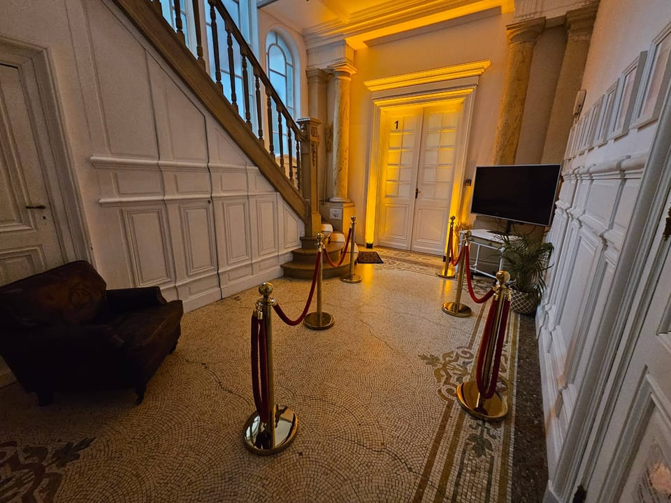 Hall d'entrée du 119 éclairé en doré, cordons de velours rouge et escalier de bois
