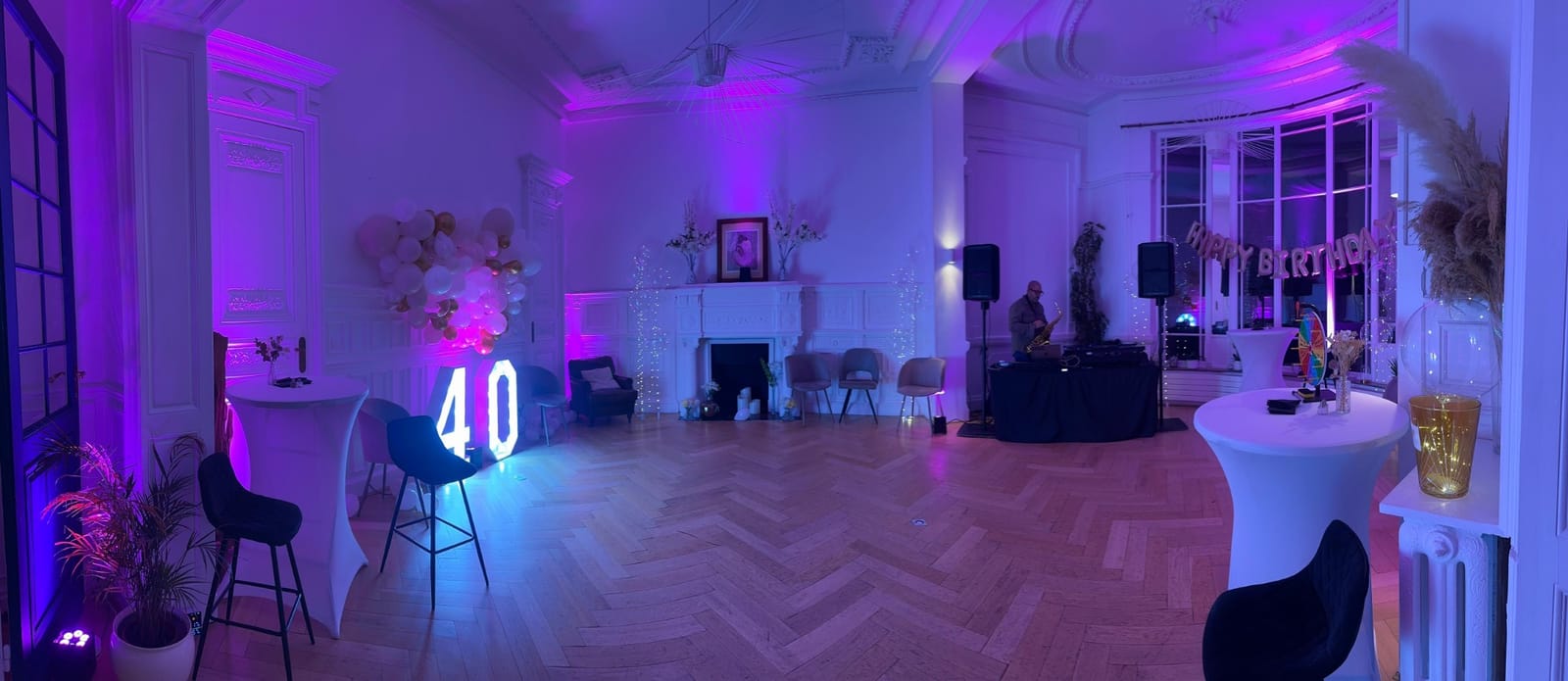 La salle de réception le soir : éclairages violets, chiffre 40 lumineux, guirlande Happy Birthday et DJ devant la baie vitrée