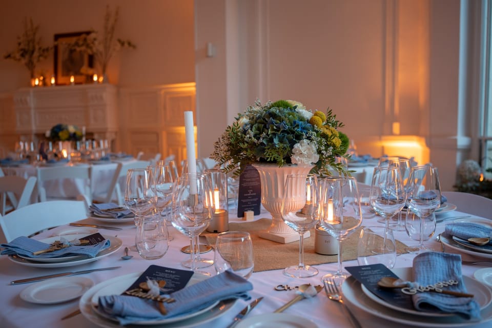 Table ronde dressée pour le dîner : bouquet d'hortensias bleus dans une vasque blanche, bougies et serviettes bleues, dans la lumière ambrée du salon