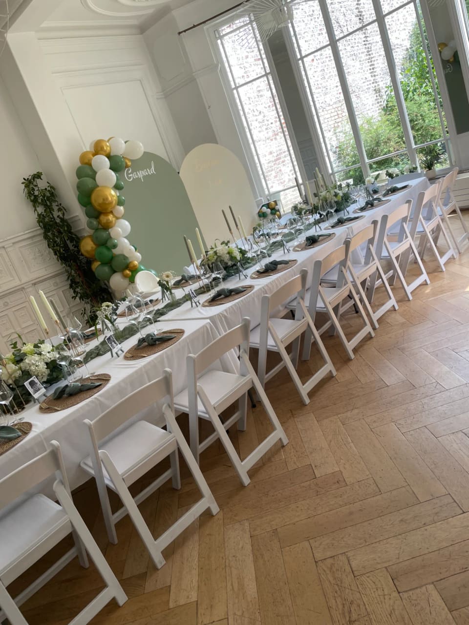 Longue table de banquet sous une arche de ballons verts et dorés