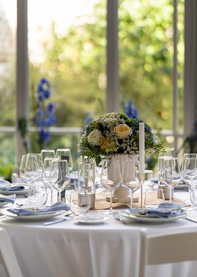 Table ronde dressée devant les baies vitrées du 119 : bouquet bleu et blanc, verres et serviettes bleues