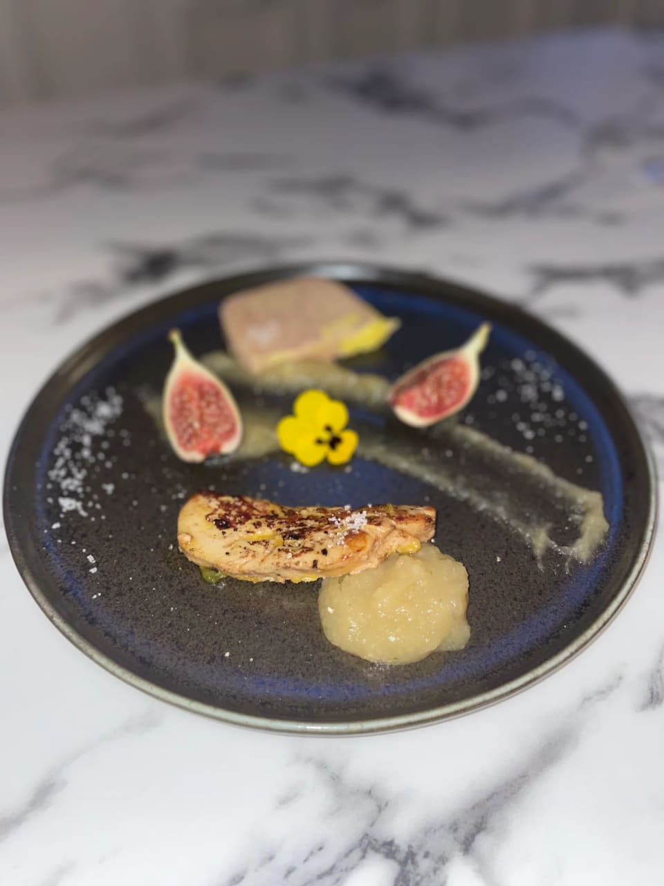 Foie gras, figues fraîches et fleur comestible sur assiette noire