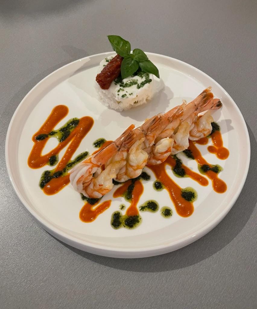 Gambas grillées et sauce au poivron, pesto et risotto, assiette dressée par le chef