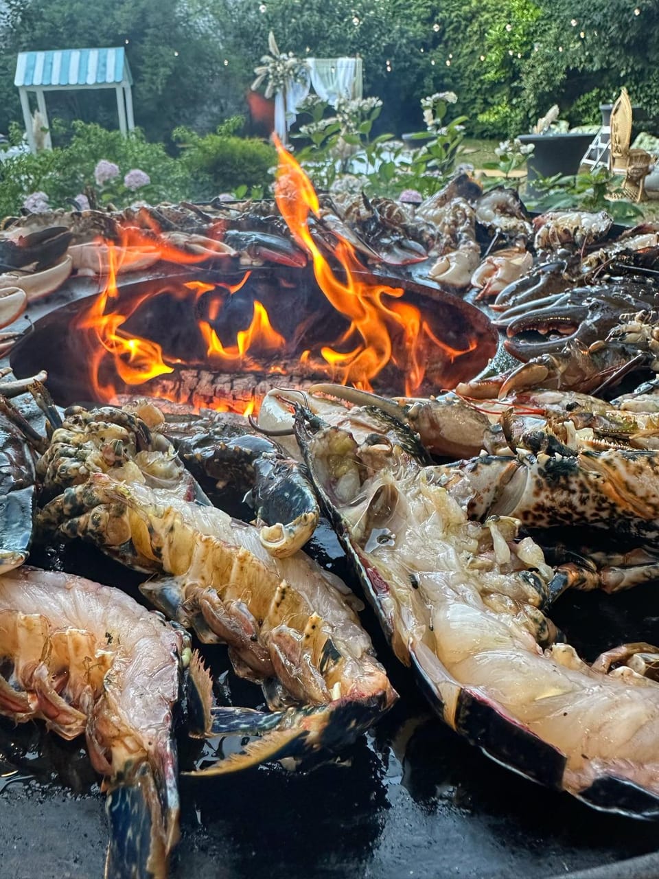Homards et fruits de mer grillés sur un brasero aux flammes vives, dans le jardin du 119