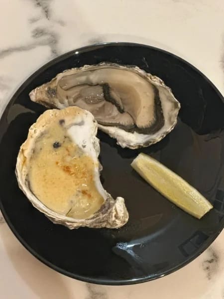 Huître gratinée et huître nature servies sur assiette noire