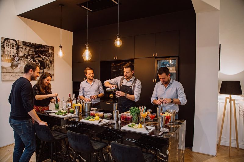 Collègues préparant des cocktails autour de l'îlot en marbre de la cuisine du 119, shakers, citrons et menthe fraîche sur le plan de travail