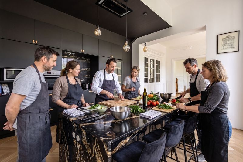 Équipe en tablier autour de l'îlot en marbre de la cuisine du 119, guidée par un chef qui découpe devant les participants