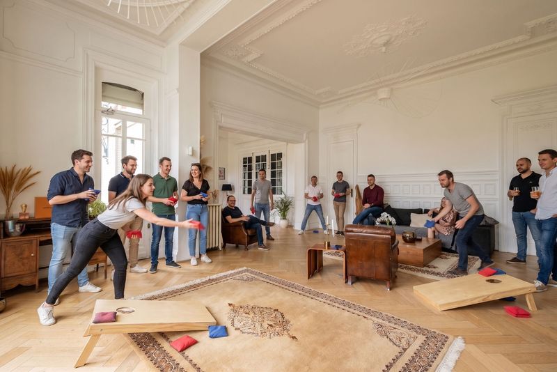 Collègues lançant des sacs de cornbag vers des planches trouées dans le grand salon du 119, sous les encouragements des autres participants