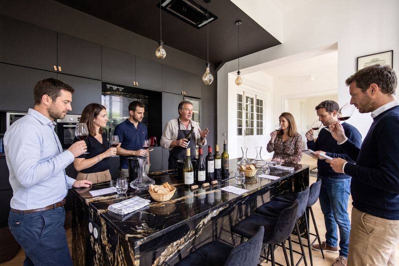 Équipe en dégustation de vins rouges autour de l'îlot en marbre de la cuisine du 119, guidée par un œnologue qui présente les bouteilles
