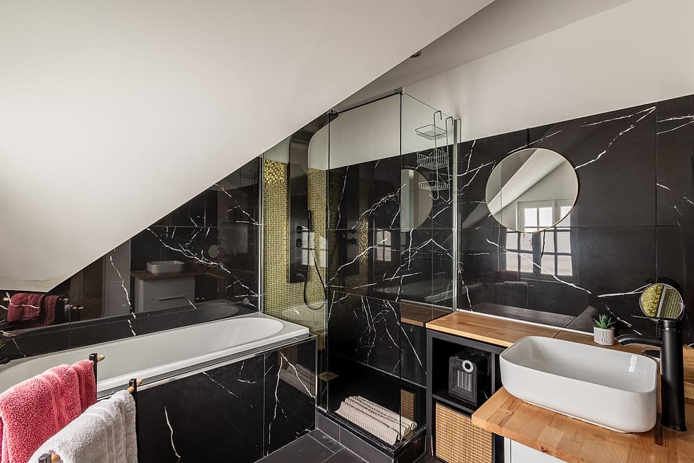 Salle de bain avec baignoire, marbre noir et miroir rond, appartement #3 du 119