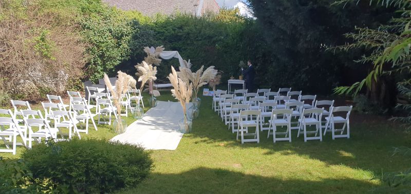 Cérémonie laïque dans le jardin du 119 : chaises blanches, allée et arche décorée d'herbes de la pampa