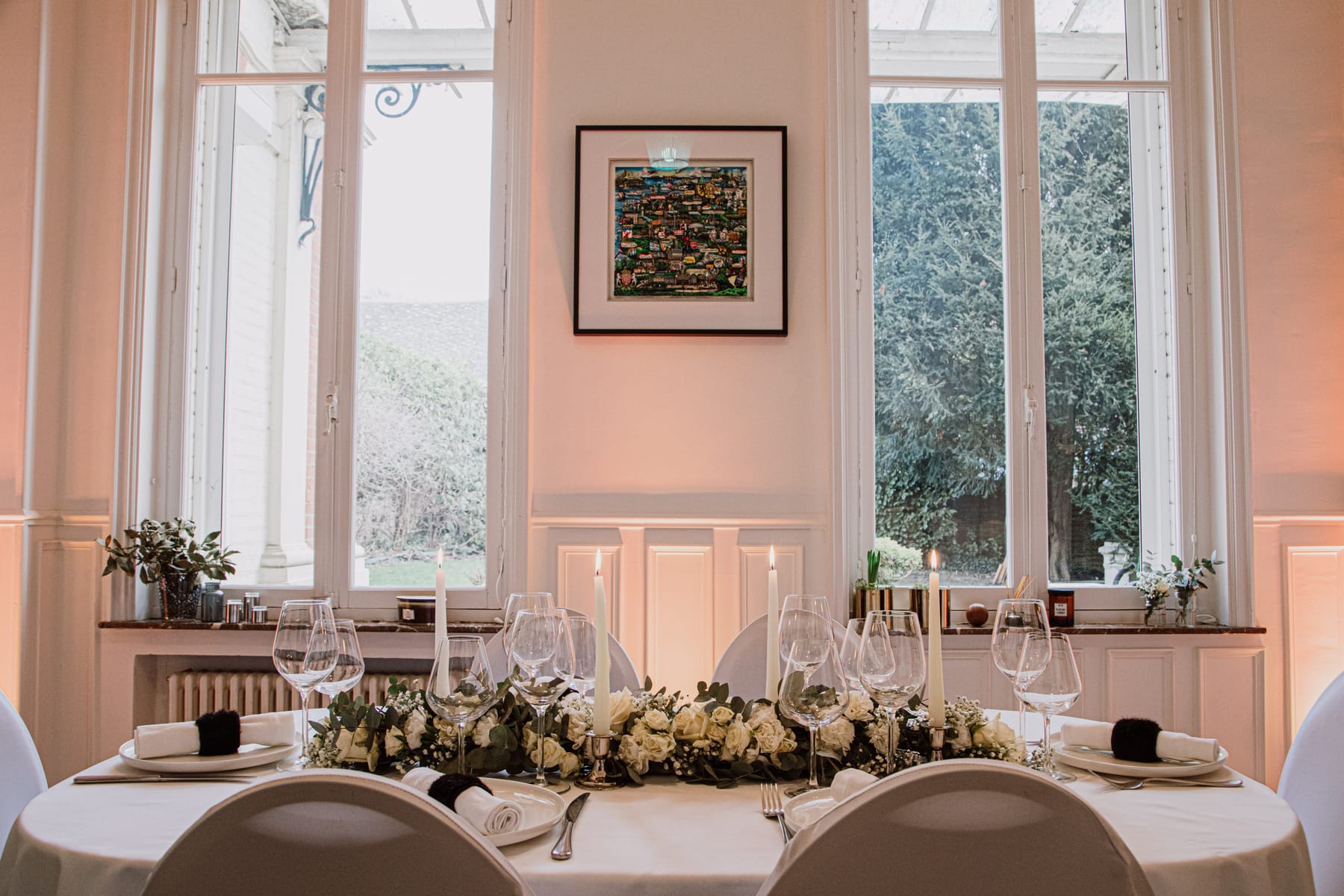 Table d'honneur dressée pour un mariage à l'hôtel particulier Le 119 : chandeliers, guirlande de roses blanches et grandes fenêtres sur le jardin