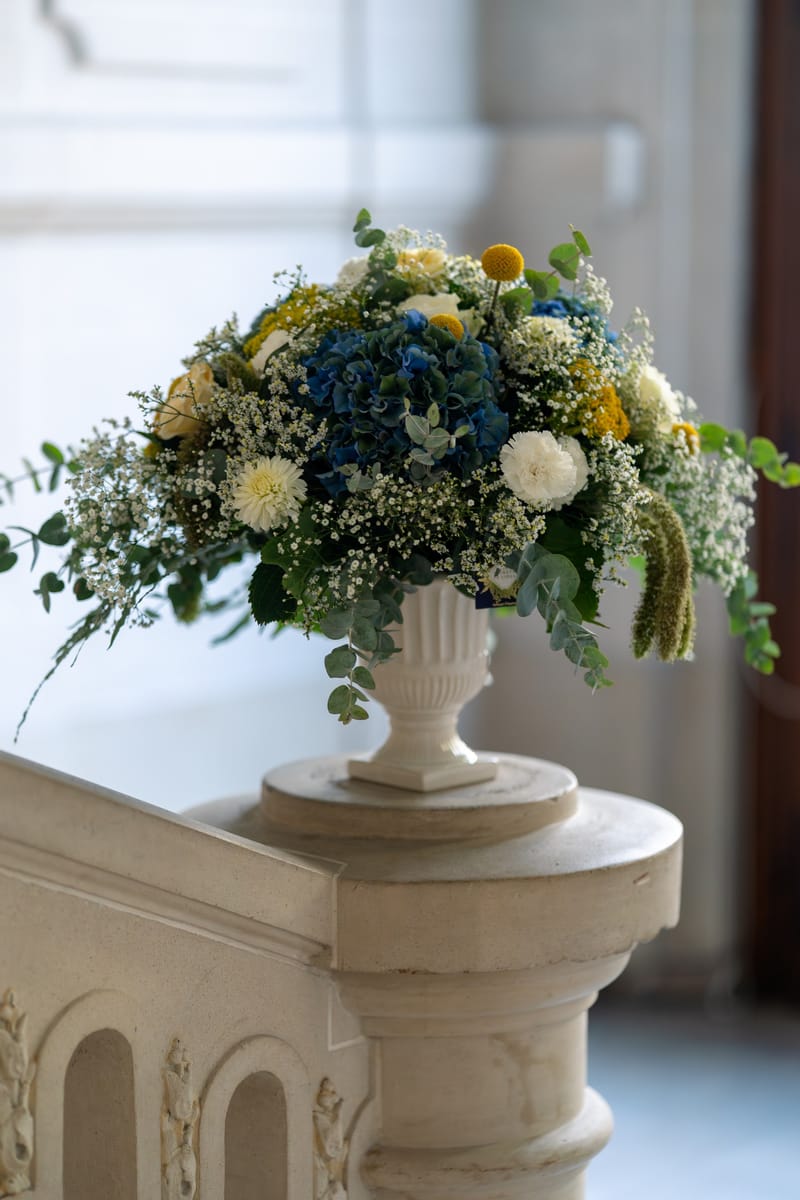 Bouquet bleu, jaune et blanc dans une urne sur la rampe de l'escalier