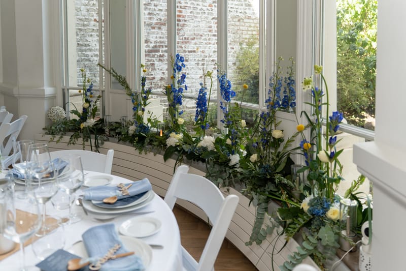 Delphiniums bleus et roses blanches le long de la baie vitrée du salon